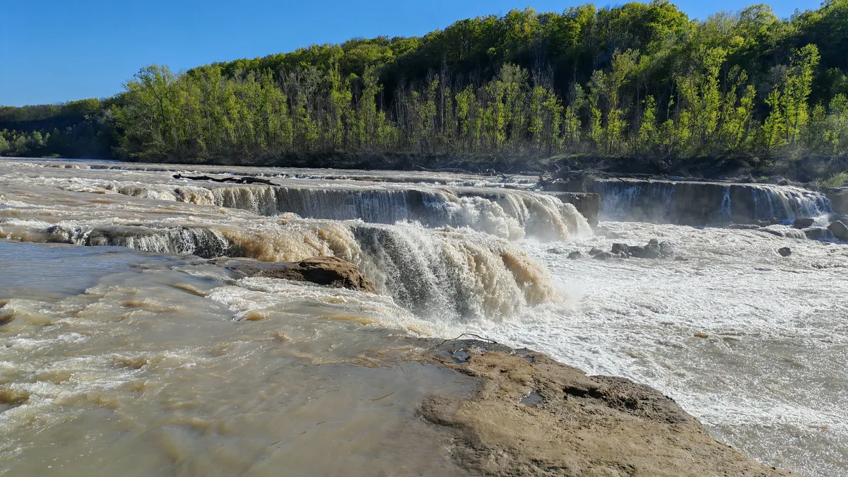 Вода падает с каменных уступов в белую пену у Белореченского водопада.